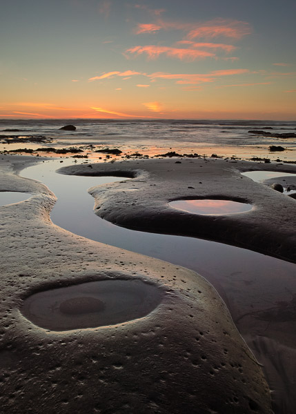 Unique shapes dominate the shoreline during low tide, while the last light of the day paints the clouds pink.