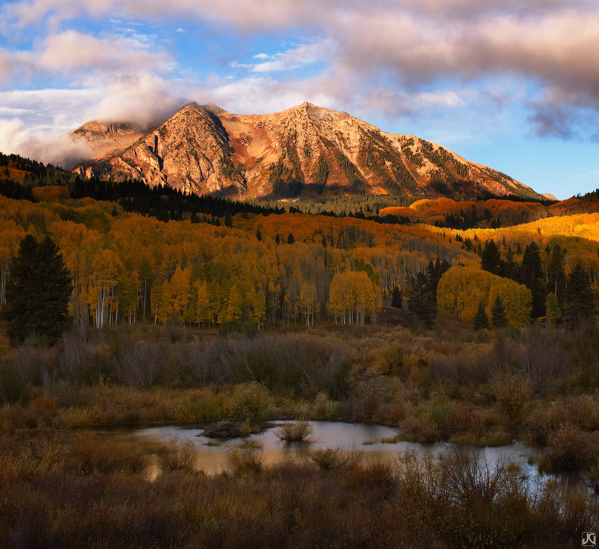 East Beckwith Mountain sits in between low morning clouds and a gold autumn aspen forest just after sunrise near Kebler Pass...
