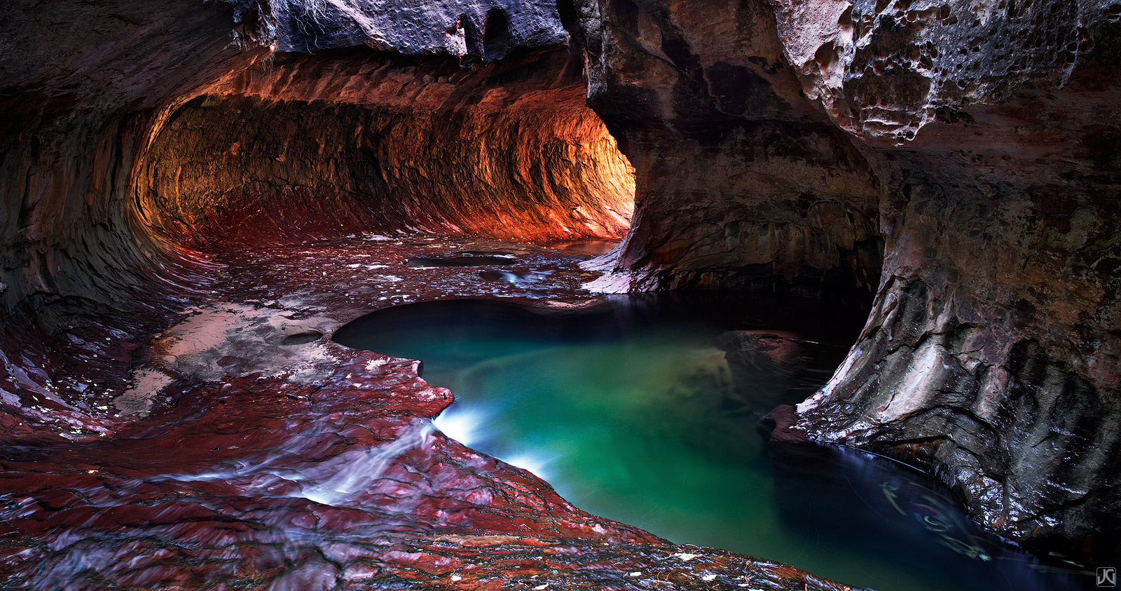 Warm light shines in on the cold, green pools at the end of the Subway along a creek in Zion's backcountry.