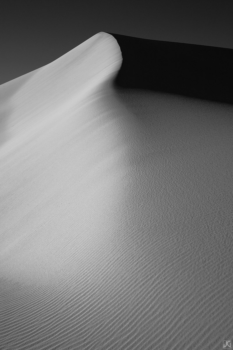 Beneath the shadows of this sand dune, the strong side light of sunrise shows the delicate patterns and lines that are formed...