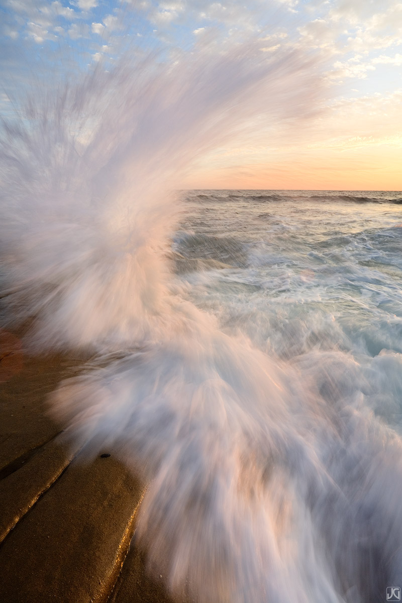 Waves crashing onto sea shelf on the coast near La Jolla, California, shimmer in the soft light of sunset.