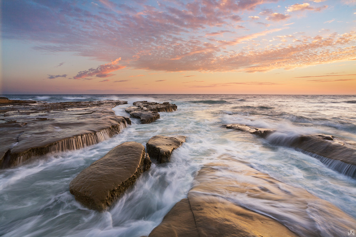 Incoming tide waters flow into channels and over the sea shelf to form small, infrequent waterfalls. The clouds during this sunset...