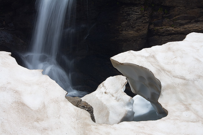 A small waterfall flows above and then beneath a snowdrift in the Porphyry Basin.