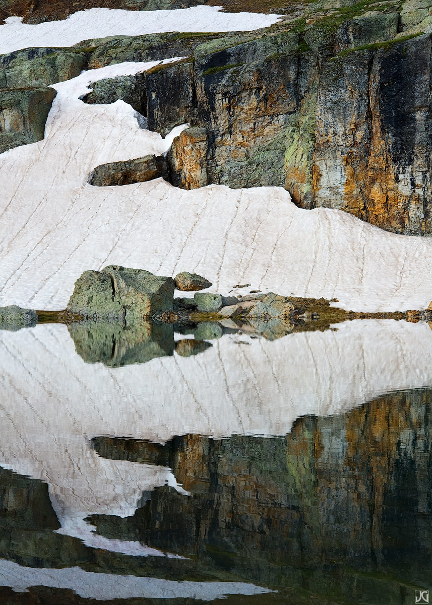 Rocks, snow and colorful streaks are reflected in Bullion King Lake.