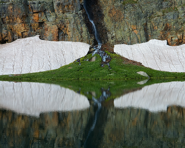 Rocks, snow and colorful streaks are reflected in Bullion King Lake.