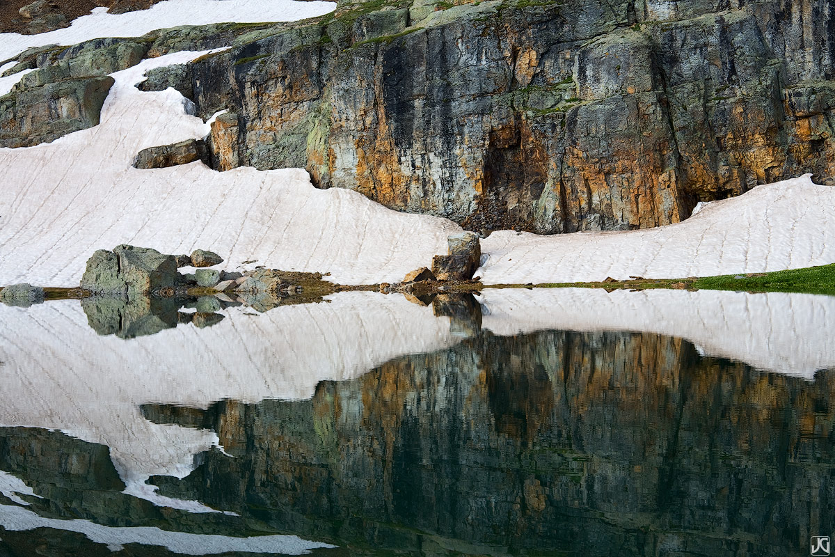 Rocks, snow and colorful streaks are reflected in Bullion King Lake.