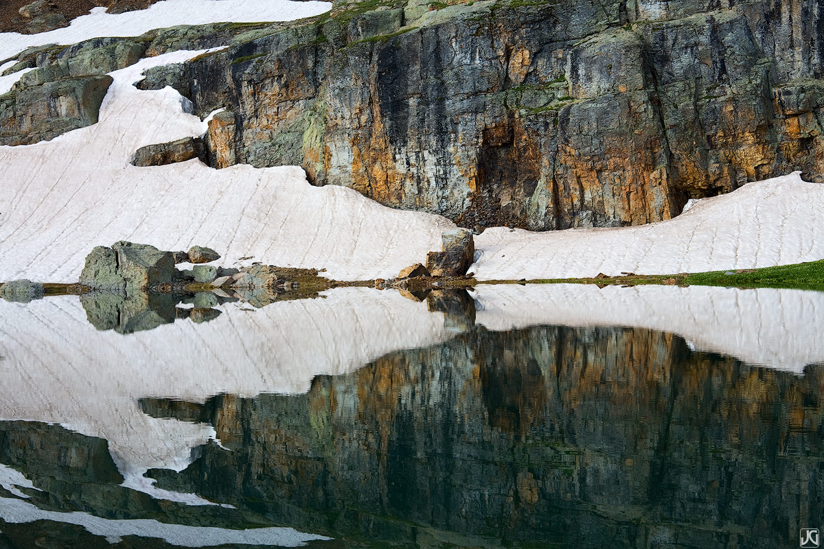Rocks, snow and colorful streaks are reflected in Bullion King Lake.
