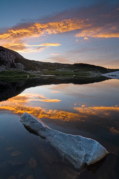 Sunrise lights up the clouds above a small tarn in the Snowy Range of Wyoming.