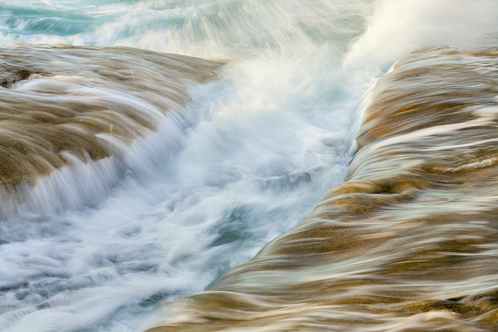The incoming rush of the sea flows over the rocks and through the channels during sunset along the coast of San Diego.