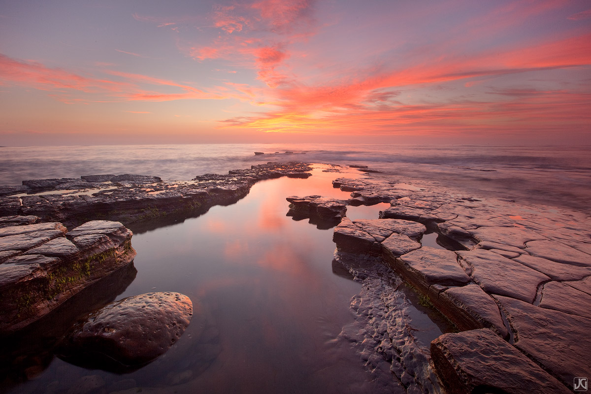 A small pool at sunset reflects the great colors in the sky along a scenic stretch of coast in San Diego.