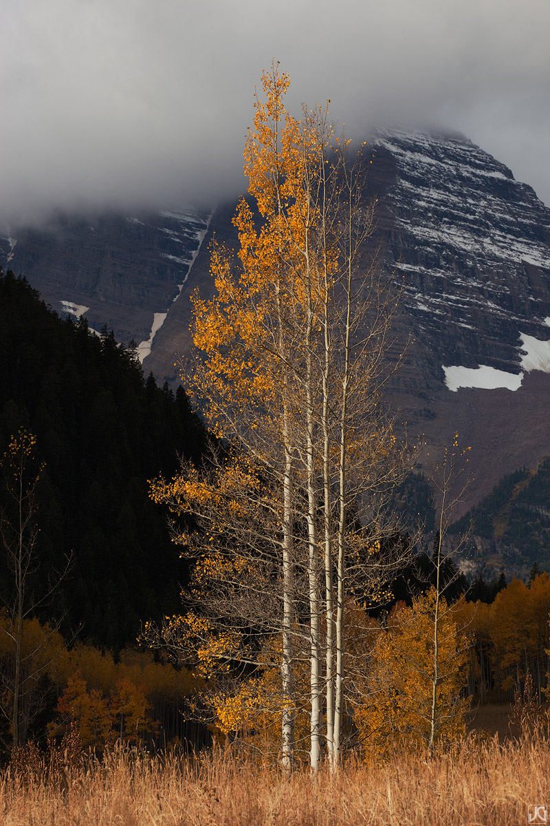 Autumn colors and aspen trees stand out against the clouds that drape over the Maroon Bells.
