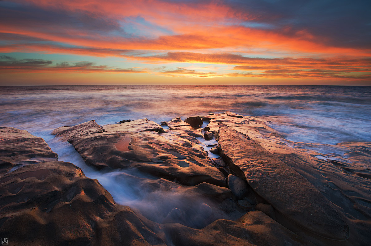 An incredible sunset lights up the sea and sky, as the irridescent light reflects on the metallic looking rocks.&nbsp;