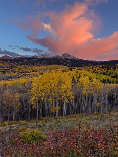 Colorful sunset clouds tower above El Diente Peak and Wilson Peak while the autumn aspen forest below show off their own glorious...