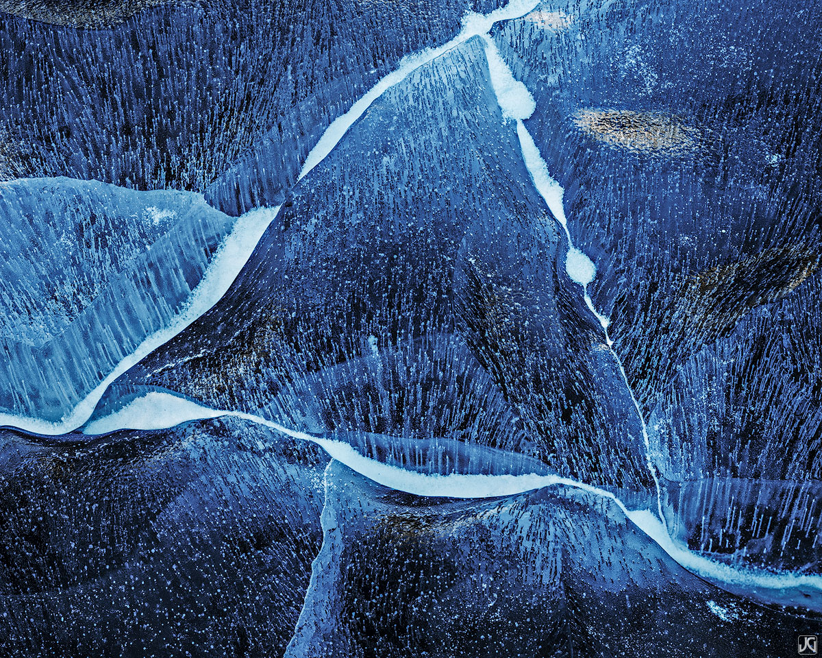 Cracks within the ice of a frozen lake form geometric shapes and unique patters.