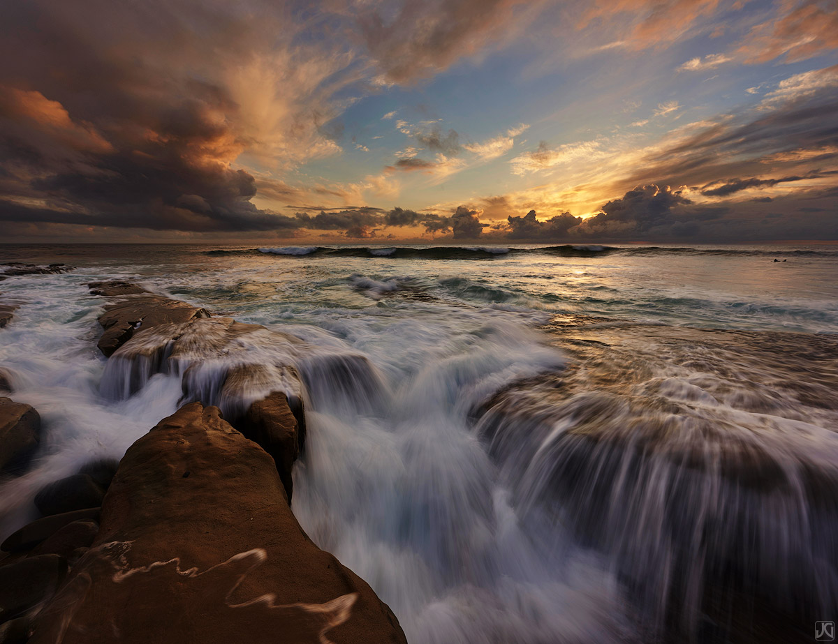 A lone surfer heads back out for a sunset session underneath some aweseome summer monsoon storm clouds.