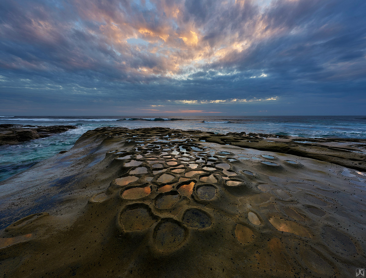 On the eve of a spring storm, sunset lights up the clouds and reflections in the potholes along the coast of La Jolla.
