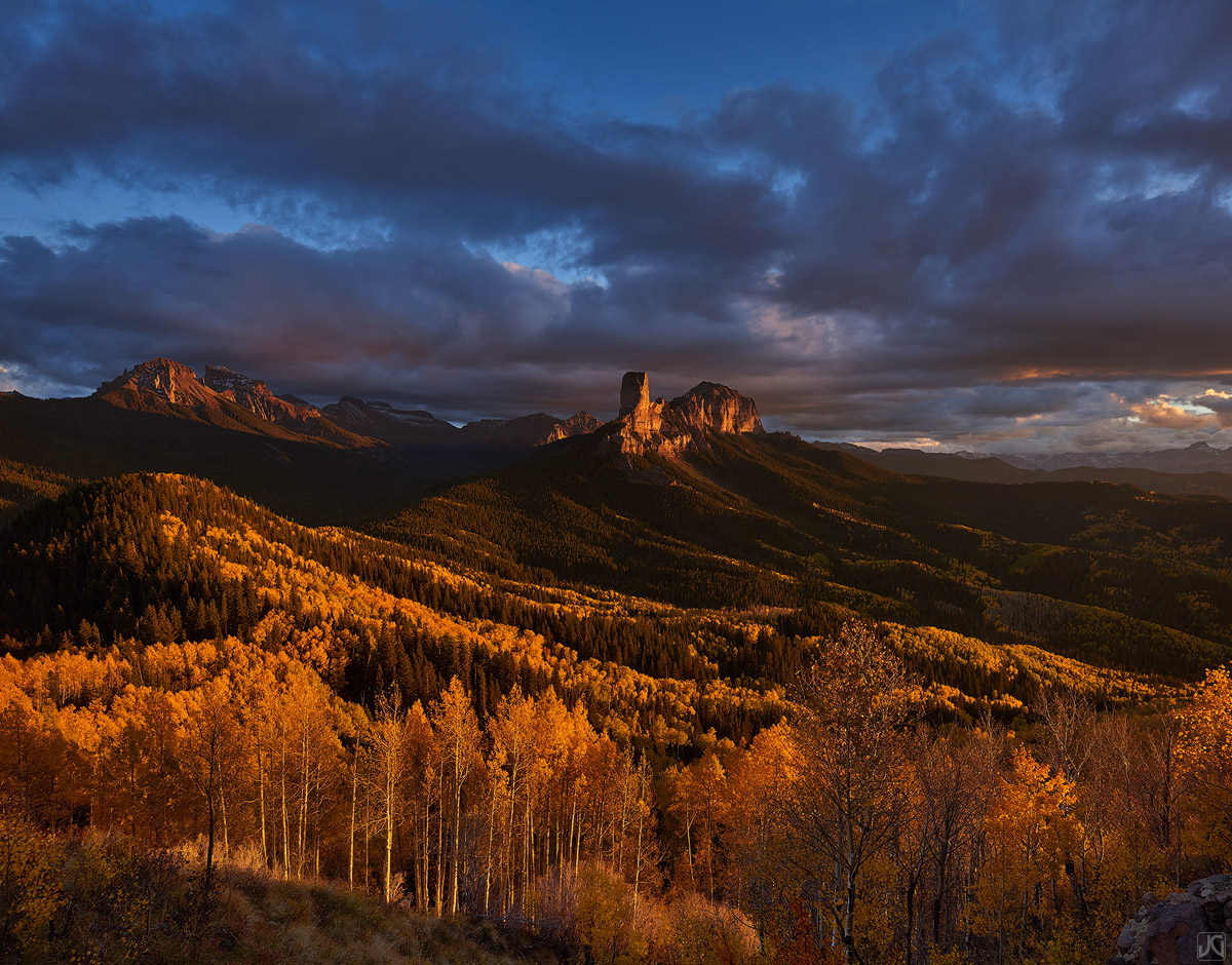 Late afternoon sunshine streams through the clouds and onto the autumn colored aspen trees.