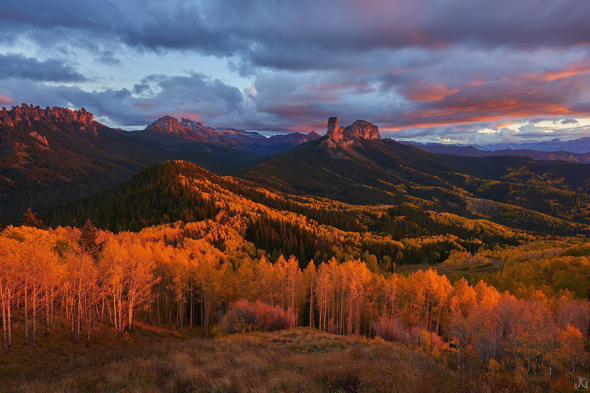 The soft light at sunset casts a vibrant glow on the clouds above and the autumn aspen trees below