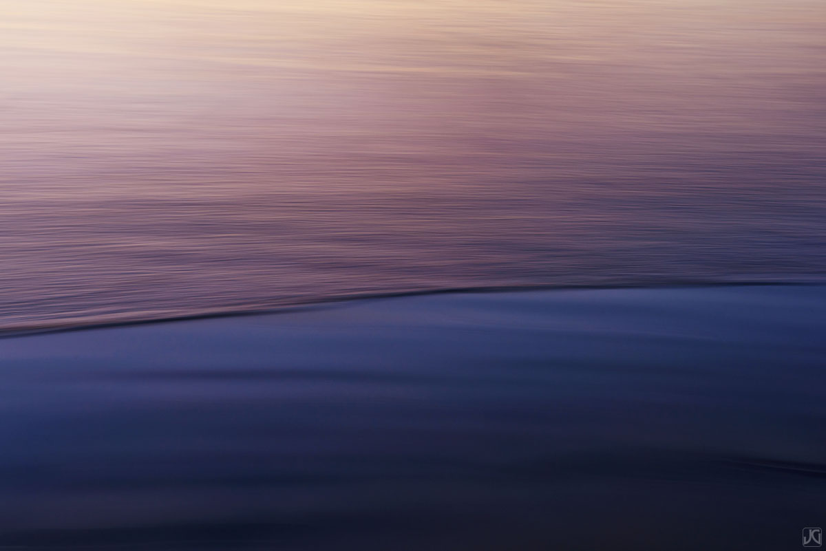 As the sky above casts a sunset glow onto the beach, the incoming sea glides across the smooth surface of the beach at low tide...