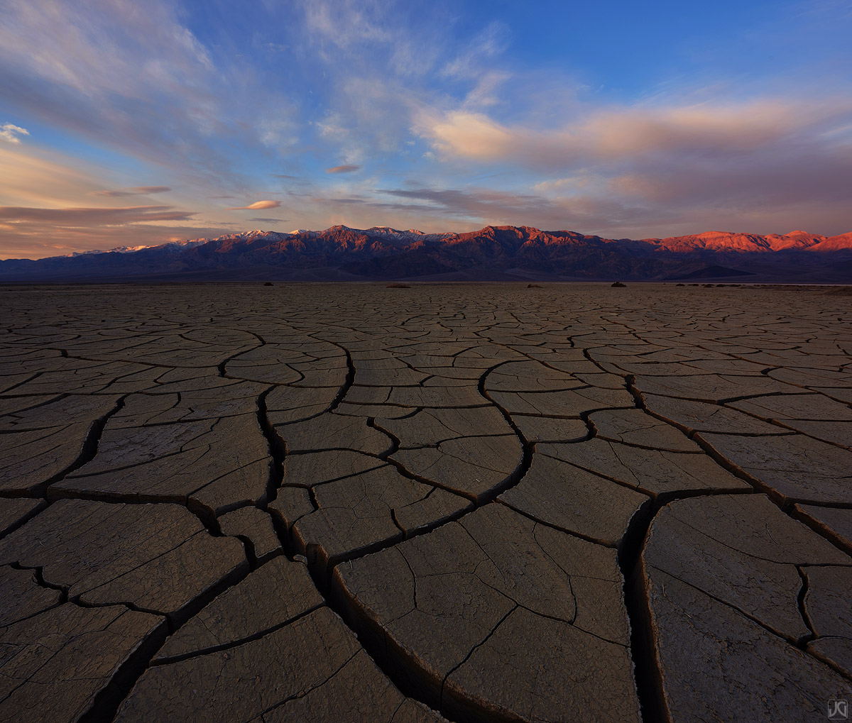 Sunrise above the mud cracks and tiles of a desert playa.