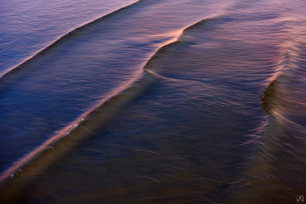 Sunset light casts the last hues of light on these small waves in the shallow waters near the coast.