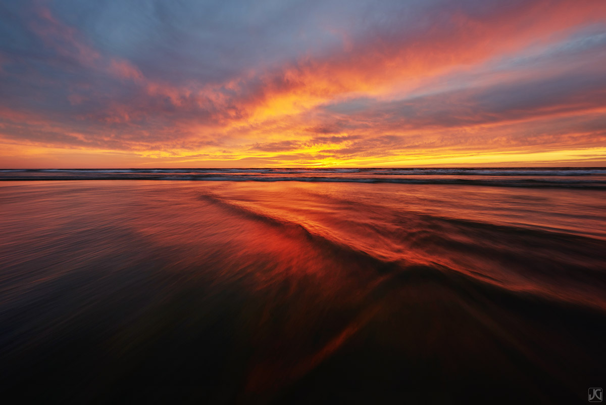 As the sunset colors the sky, the reflections and patterns of the incoming tide play on each other.