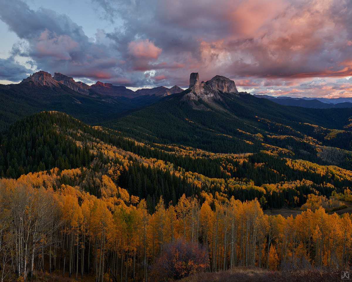The soft light after sunset casts a vibrant glow on the clouds above and the autumn aspen trees below.