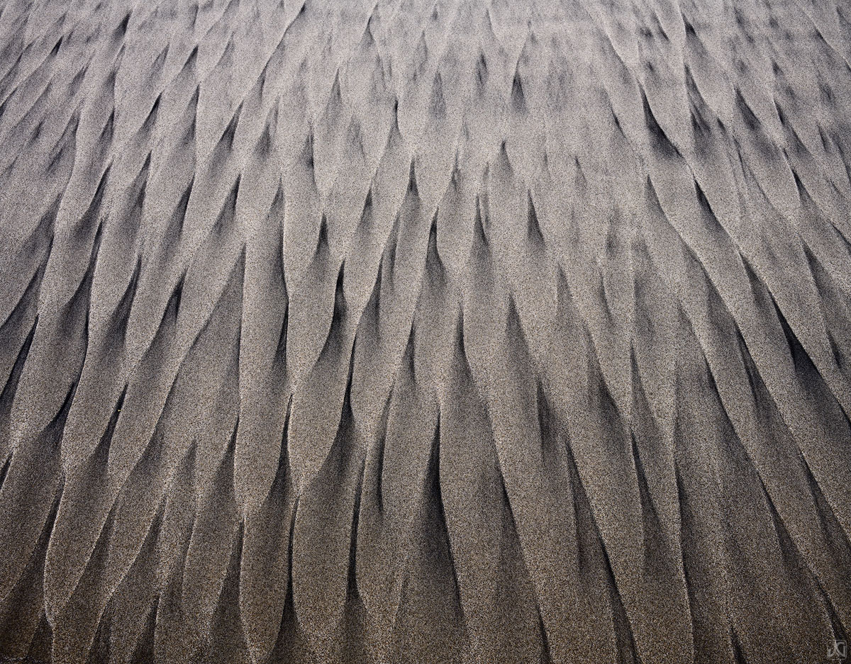 Sand and sea mix and flow towards the ocean, creating stretches of pointed patterns.