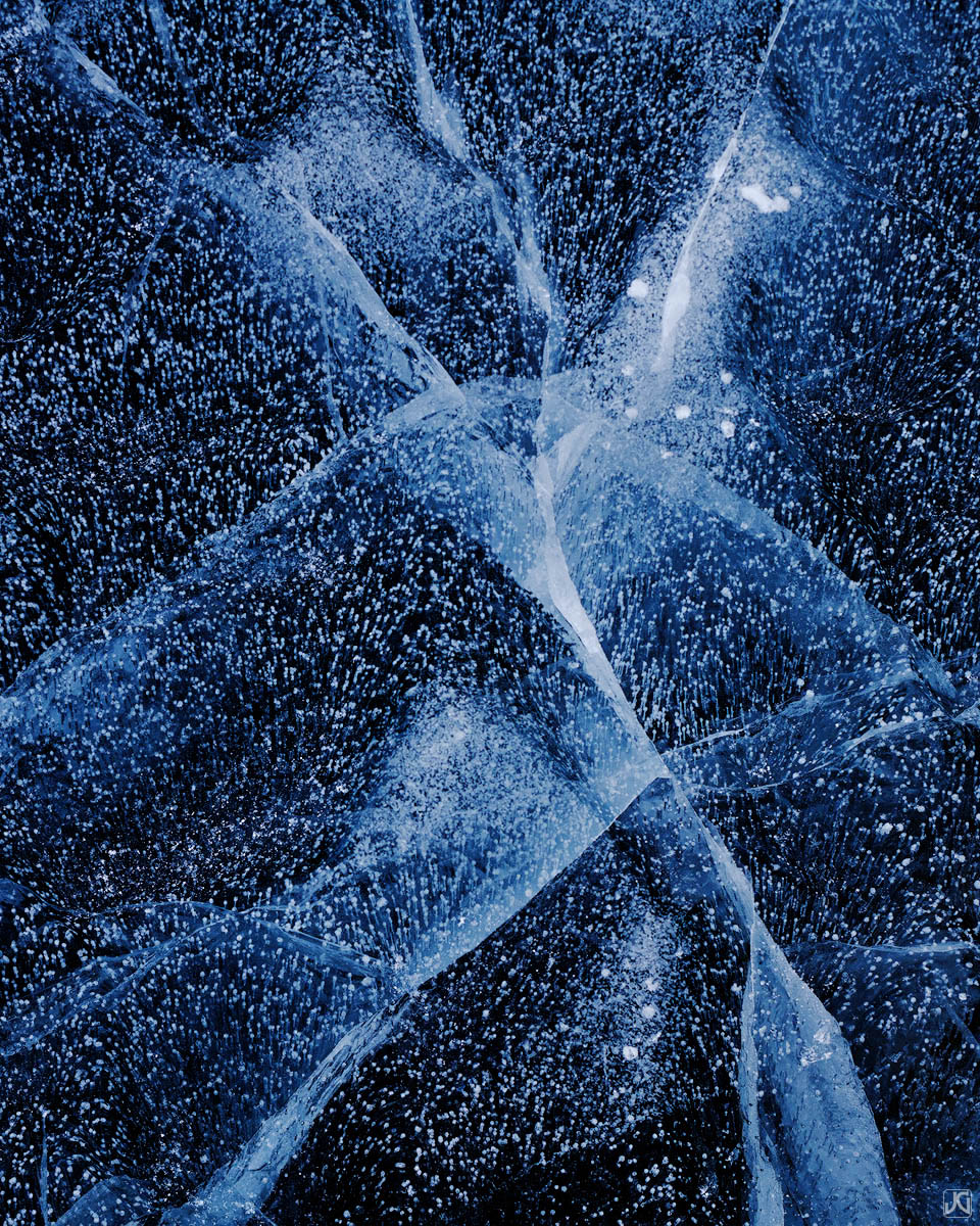 Patterns from ice cracks and bubbles on a frozen lake are akin to the clear night sky.