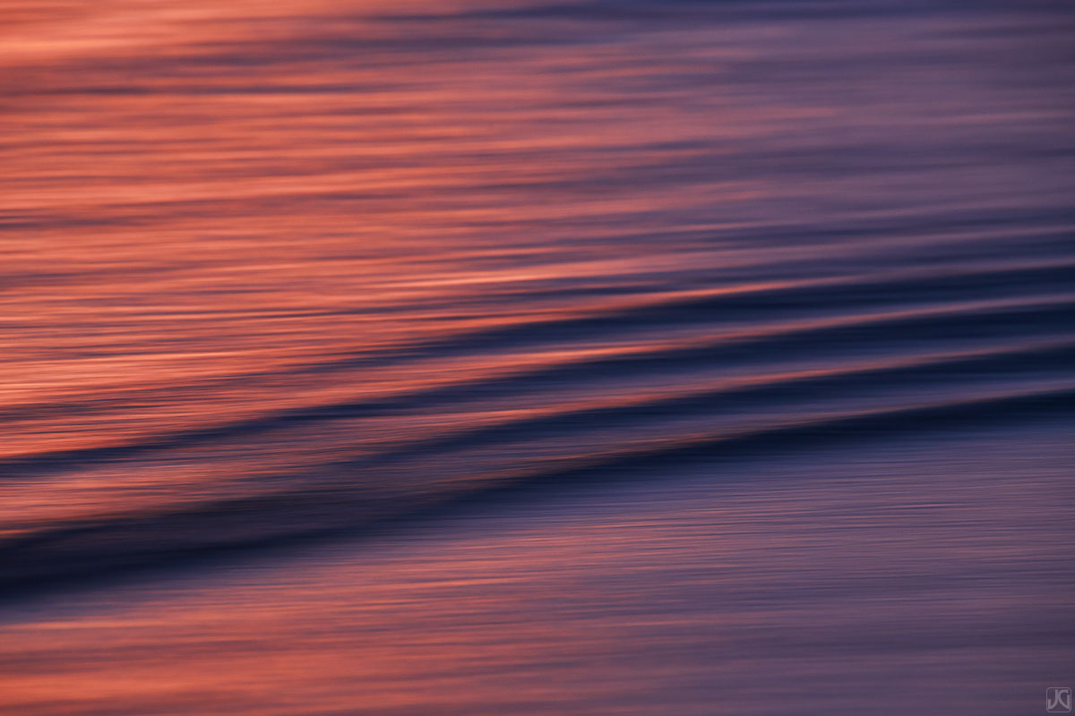 A colorful sunset bounces off the clouds above, reflecting in ripples near the coast.